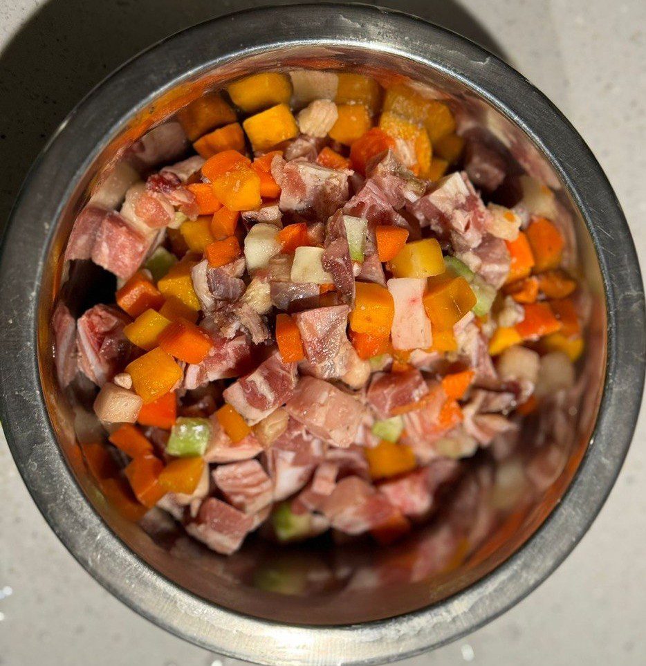 Металлическая миска сверху, доверху наполненная нарезанным кубиками мясом и овощами: морковь, кабачок, кусочки сельдерея вперемешку с кусками мяса с прослойками жира